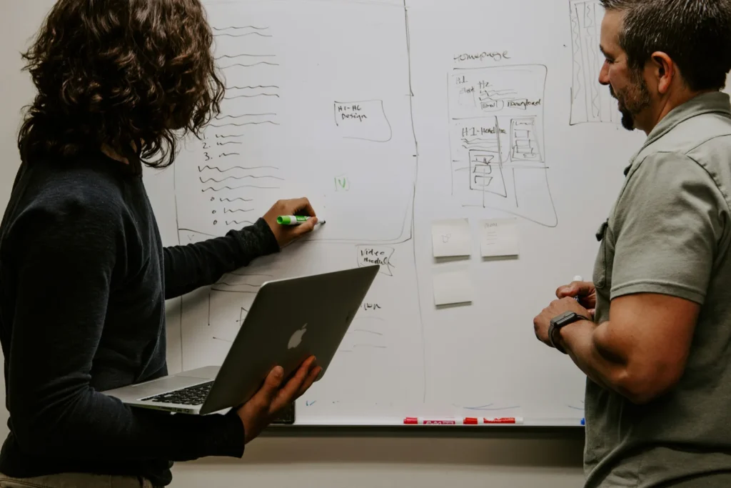 Two colleagues planning on a whiteboard with a laptop