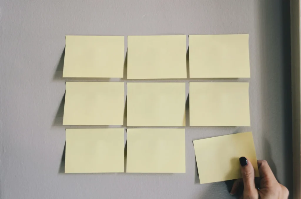 Hand arranging sticky notes in a grid on a wall
