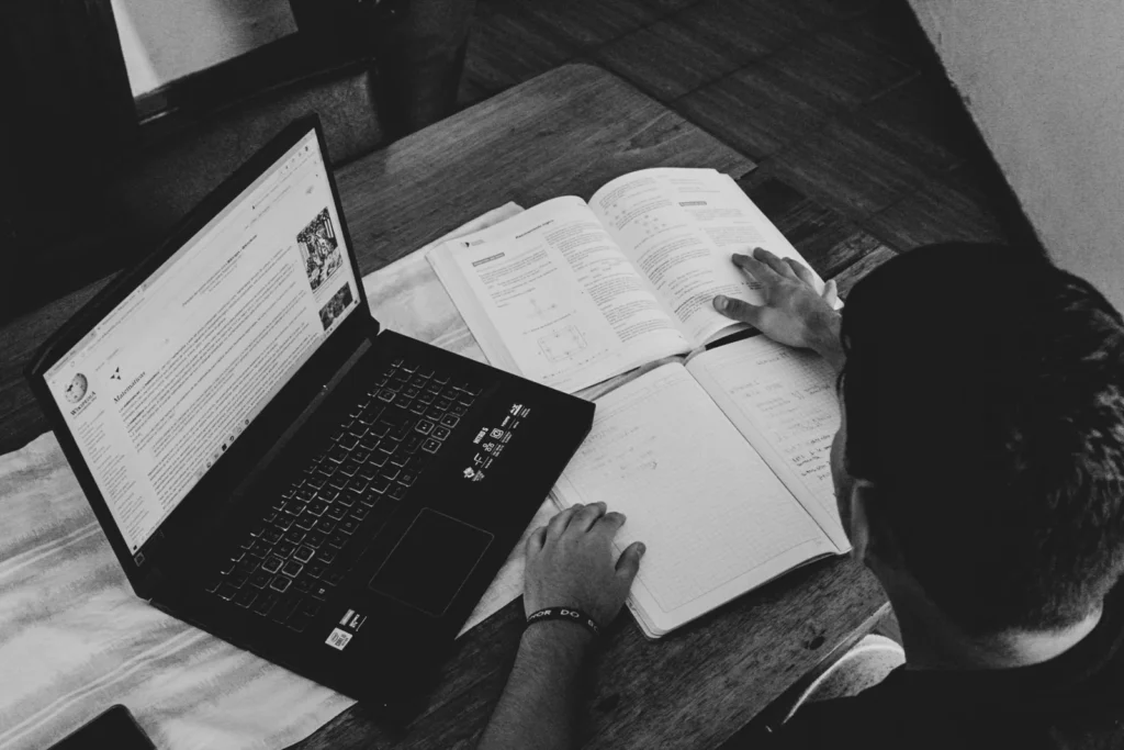 Person studying a laptop screen with an open notebook