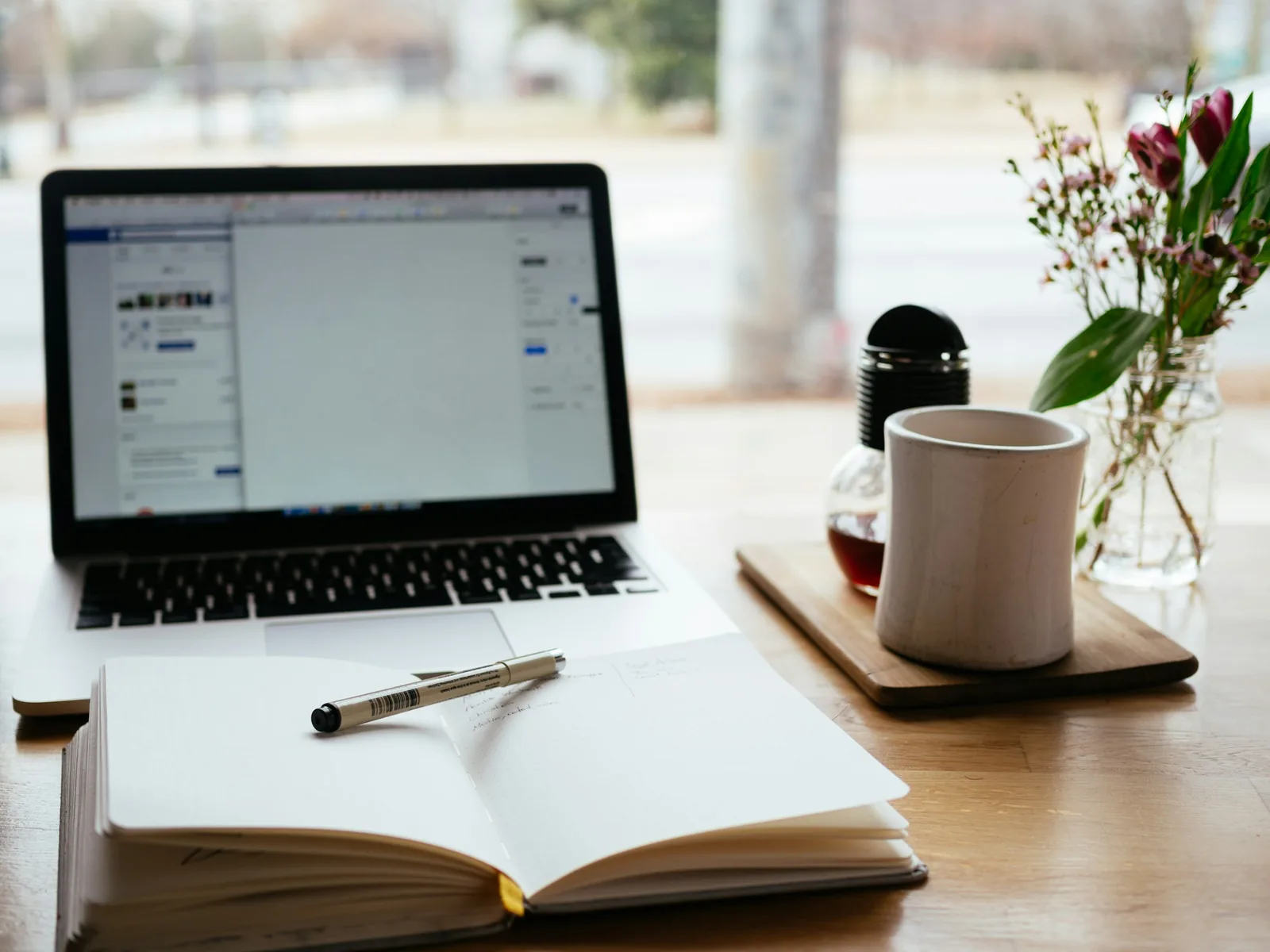Laptop and open notebook on a desk with flowers