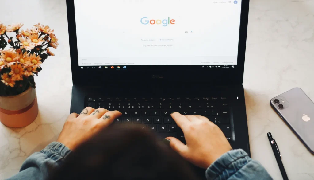 Hands typing a search on a laptop next to flowers